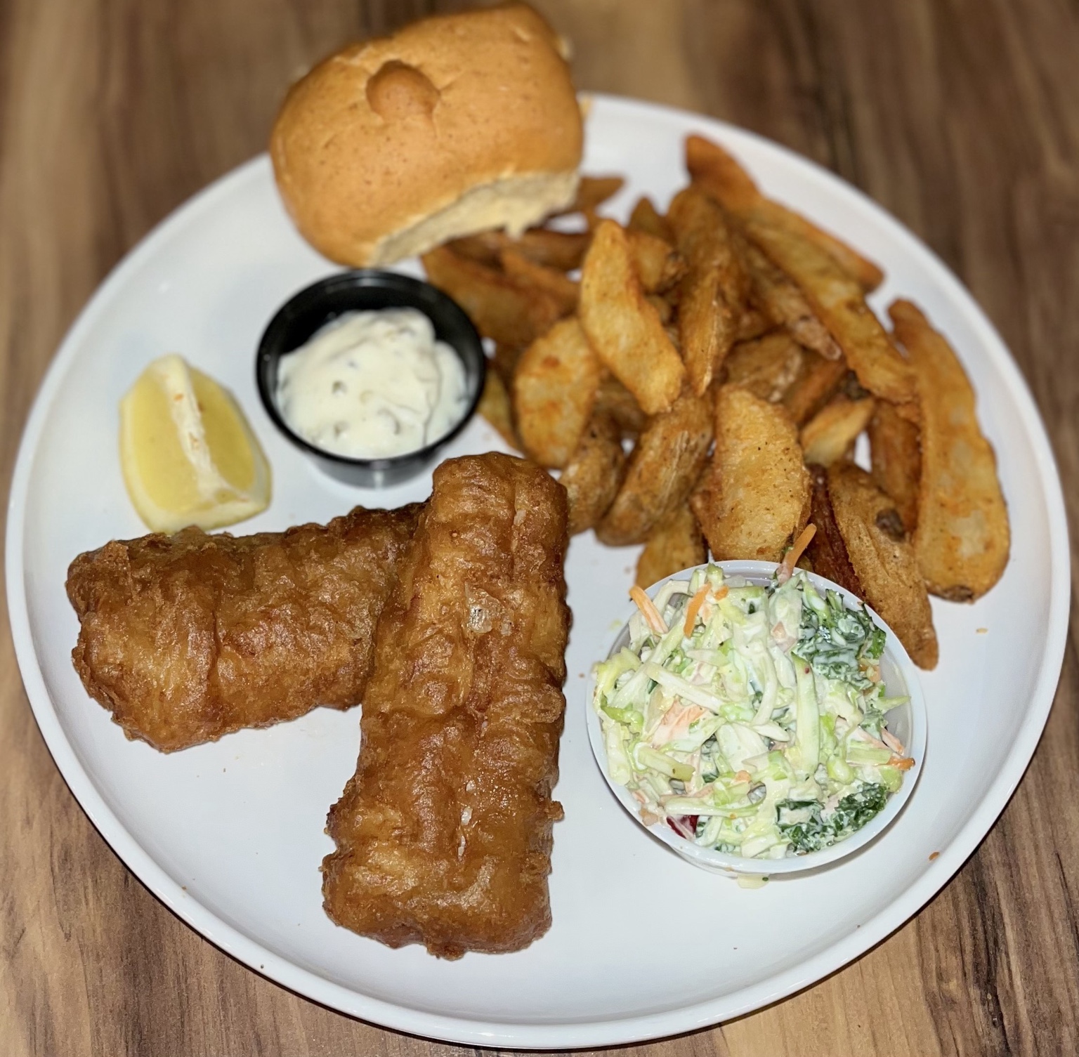 Pink Heifer cod fish fry with potato wedges, coleslaw, a roll, tartar sauce, and lemon